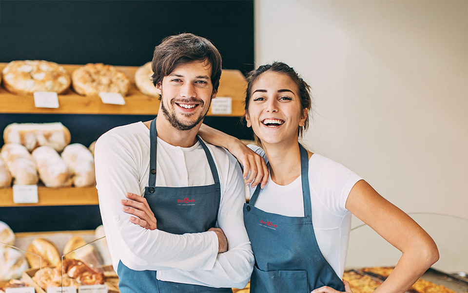 Zwei Bäckereiverkäufer vor einem Regal mit Brot
