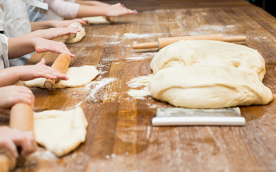 Kinder rollen ein Stück Teig an einem Tisch aus